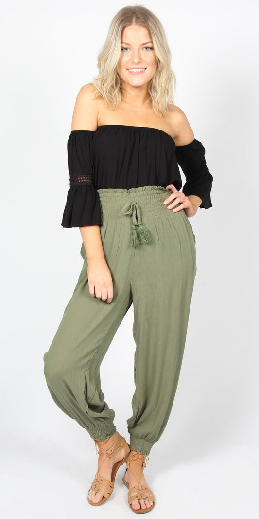 Woman wearing a black off-shoulder top and green jumpsuit on a white background